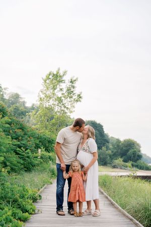 A family shares an intimate moment together on a wooden boardwalk surrounded by lush greenery on a sunny day.