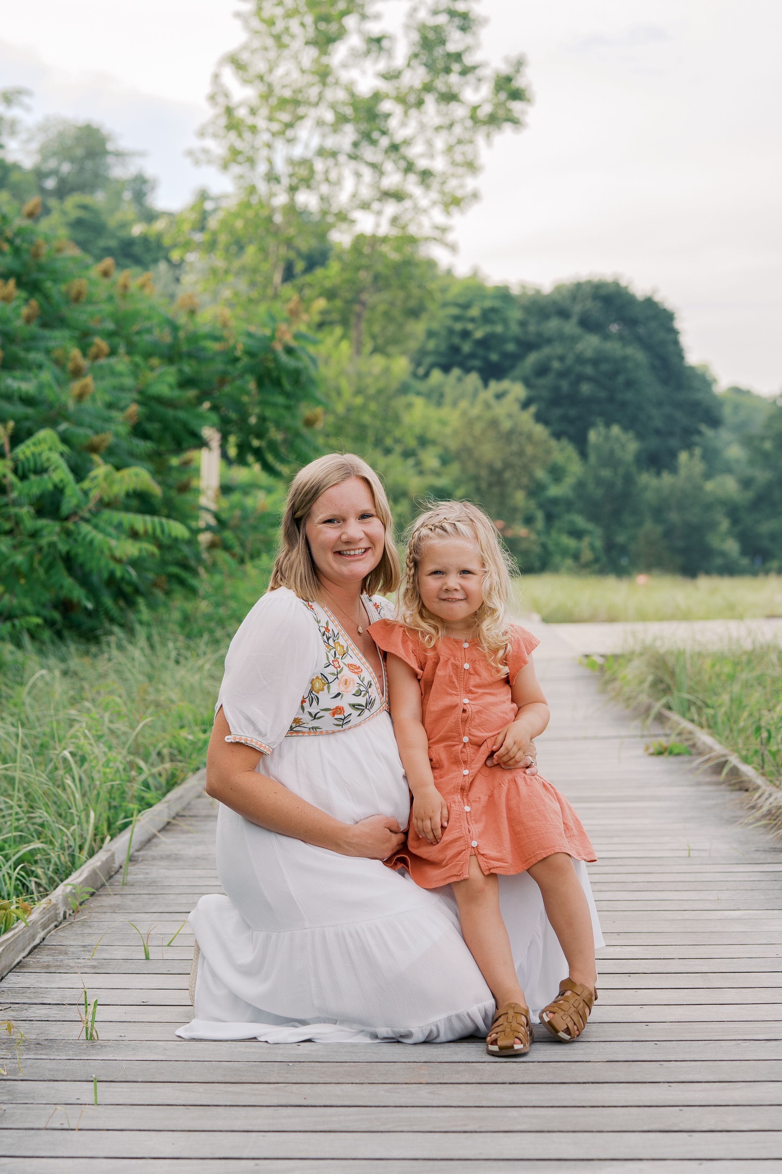 Mother and child share joyful moments together on a wooden boardwalk surrounded by lush greenery.