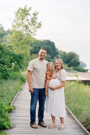 Family poses together on a wooden boardwalk surrounded by green foliage on a sunny summer day.