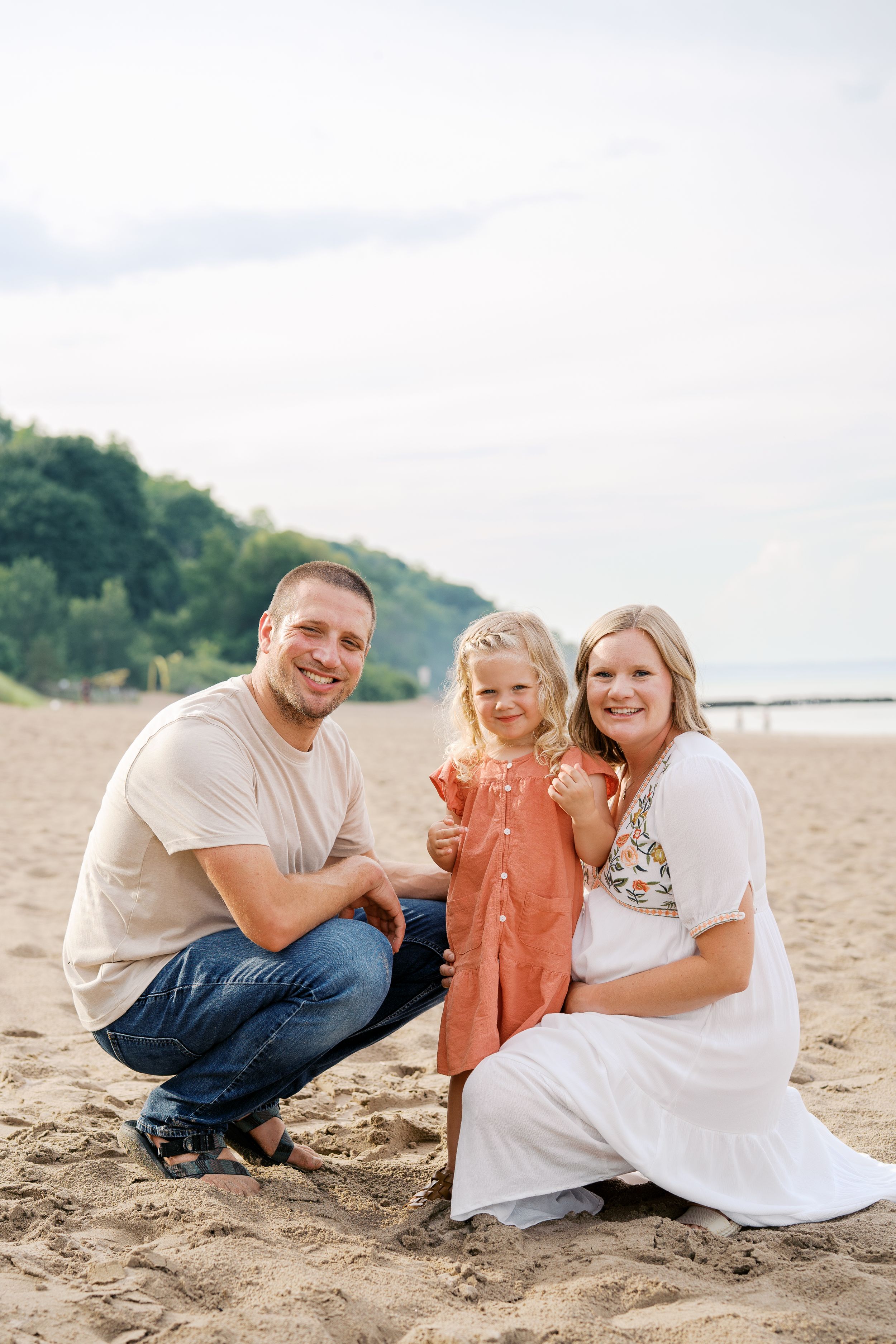 A family shares joyful moments together while sitting on a sandy beach near green hills.