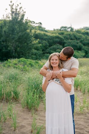 A couple shares a tender embrace in a grassy field on a sunny day.