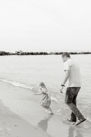 Black and white photos capture playful moments of people walking and splashing along the shoreline.