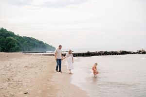 People walking and playing along a serene beach shoreline with calm waters and distant trees.