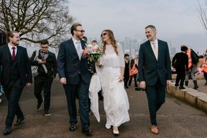 Wedding party walks together along pathway during outdoor celebration on overcast day.