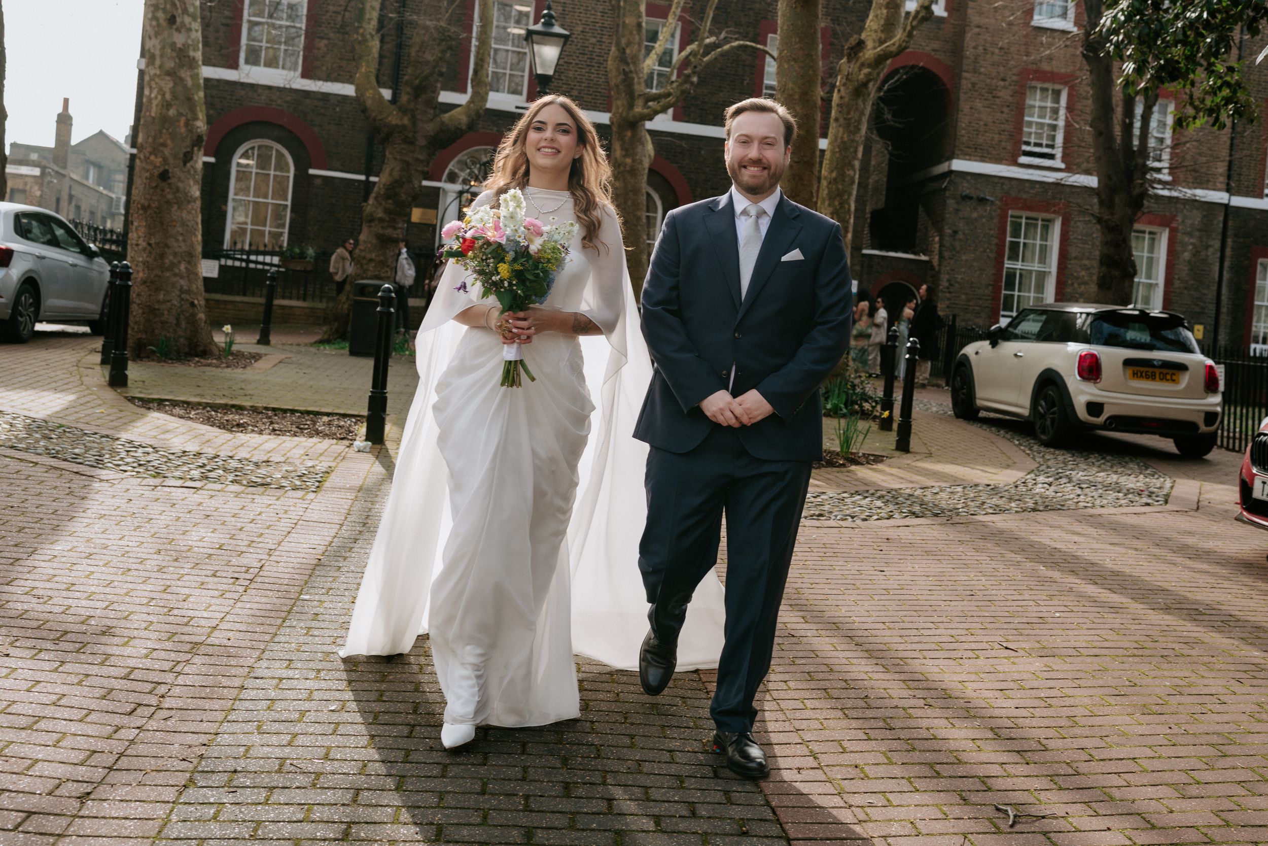 A couple walks together on a brick sidewalk outside historic brick buildings during their wedding day.