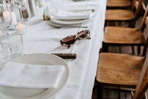 A rustic dining table set with white plates and wooden chairs against a white tablecloth.