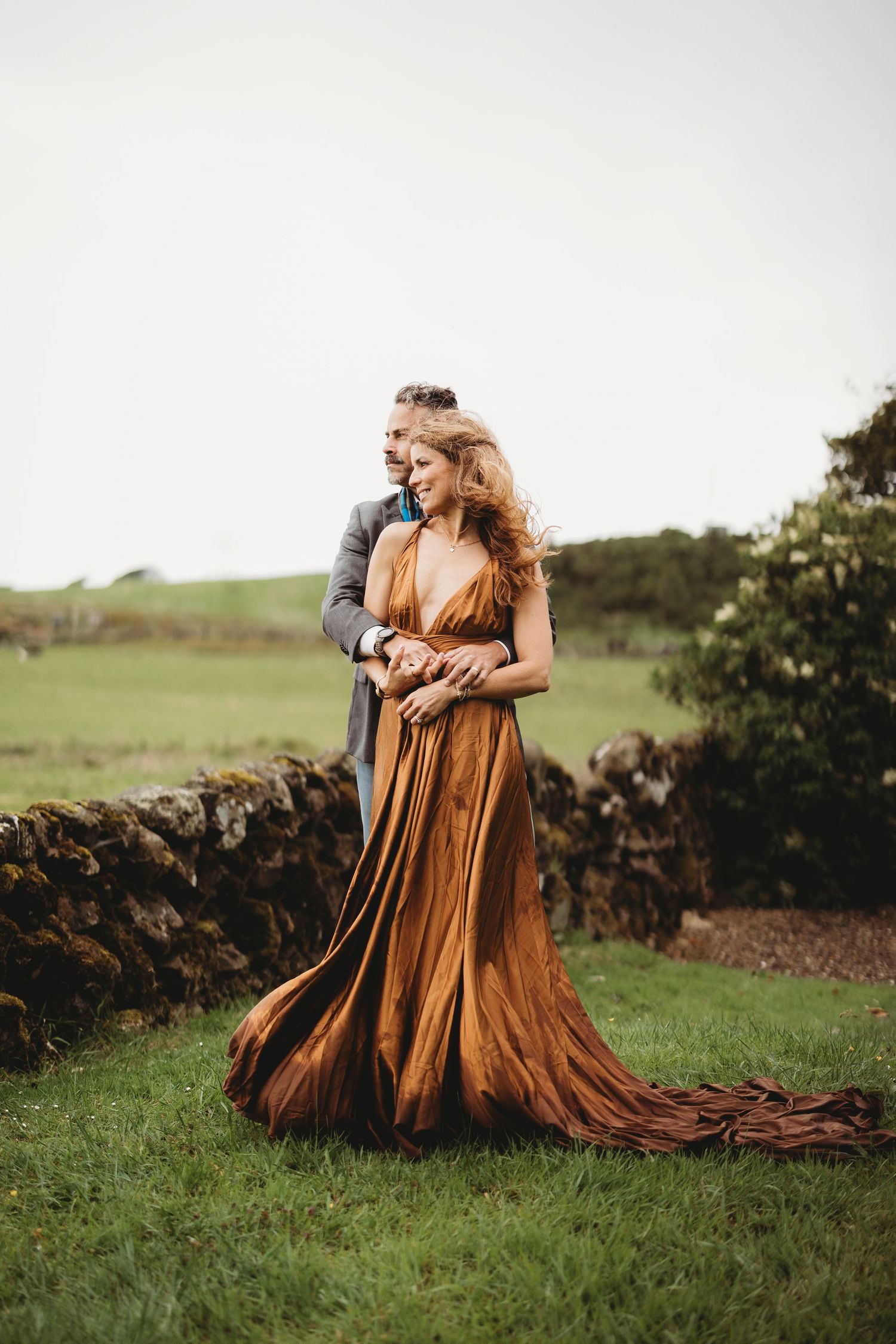 Couple gazing at a historic castle ruins across golden fields at sunset.