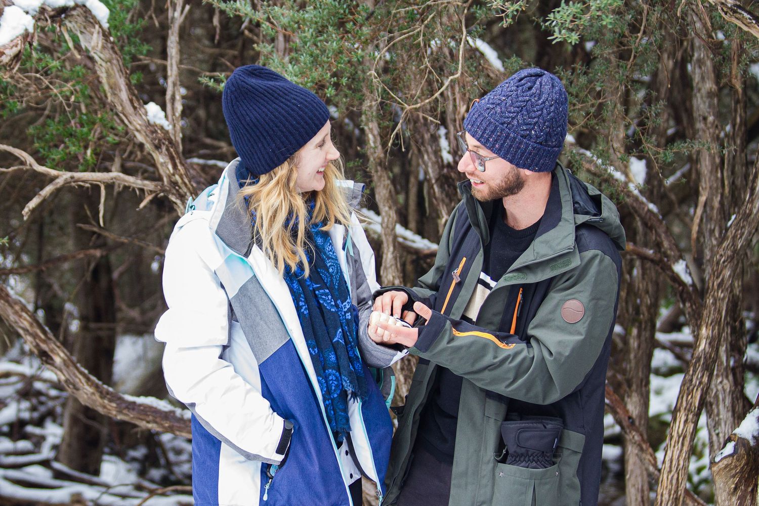 A couple embraces in a romantic outdoor proposal photoshoot against a scenic mountain landscape with natural sunlight.