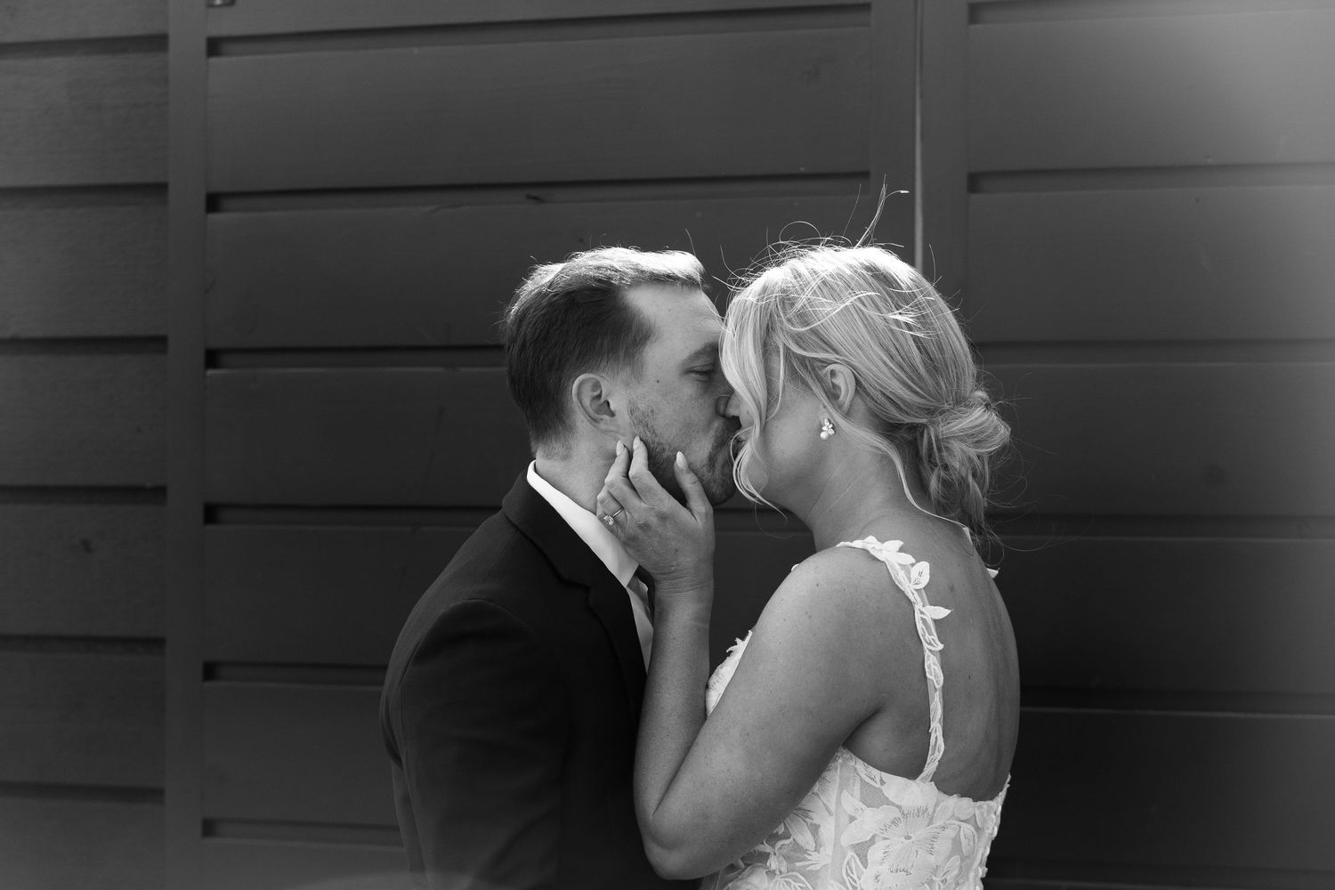 Black and white photo of a bride and groom sharing a romantic kiss on their wedding day.
