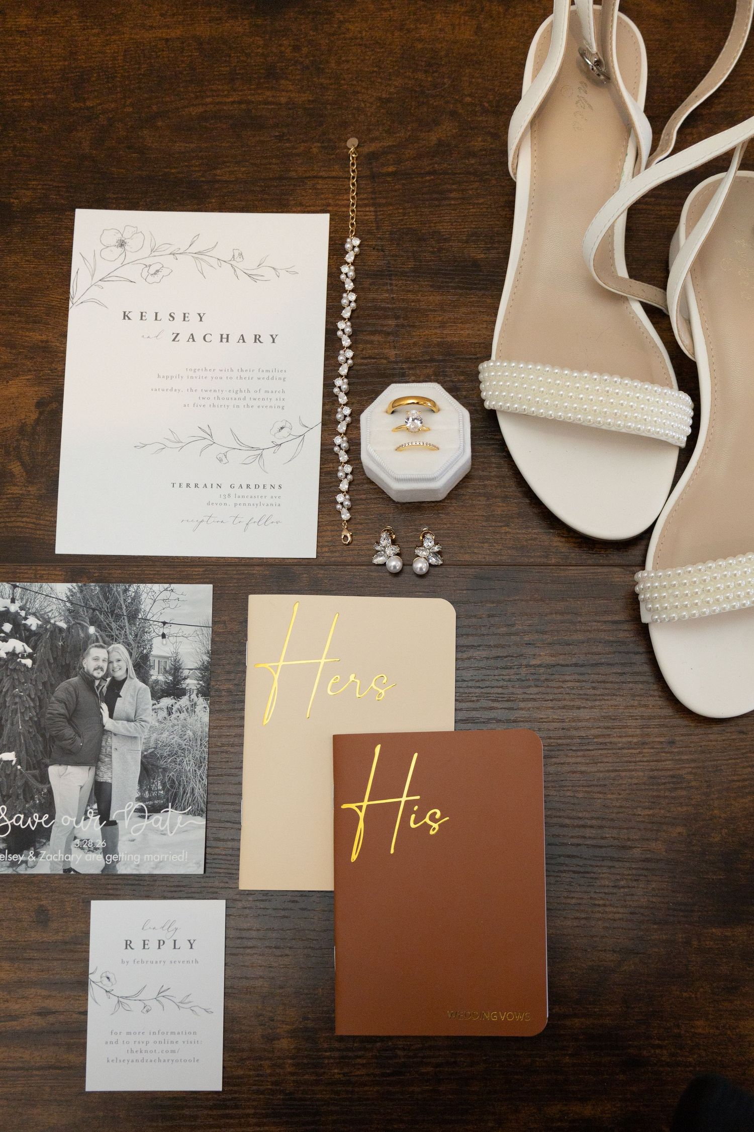 Elegant wedding flat lay with invitations, pearl heels, rings, and His & Hers vow books on wood.
