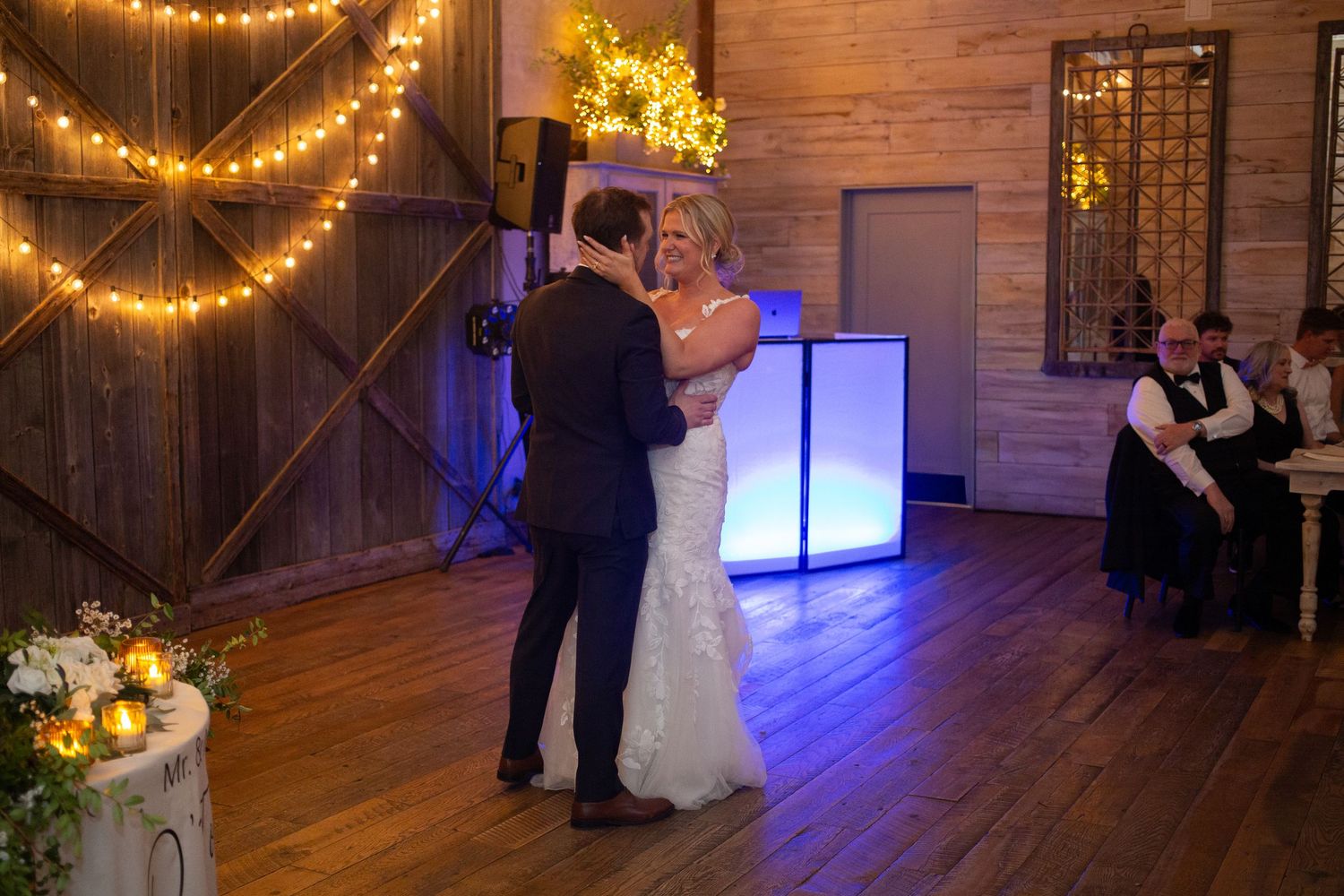 Bride and groom share their first dance in a warmly lit barn venue decorated with string lights at their wedding reception.