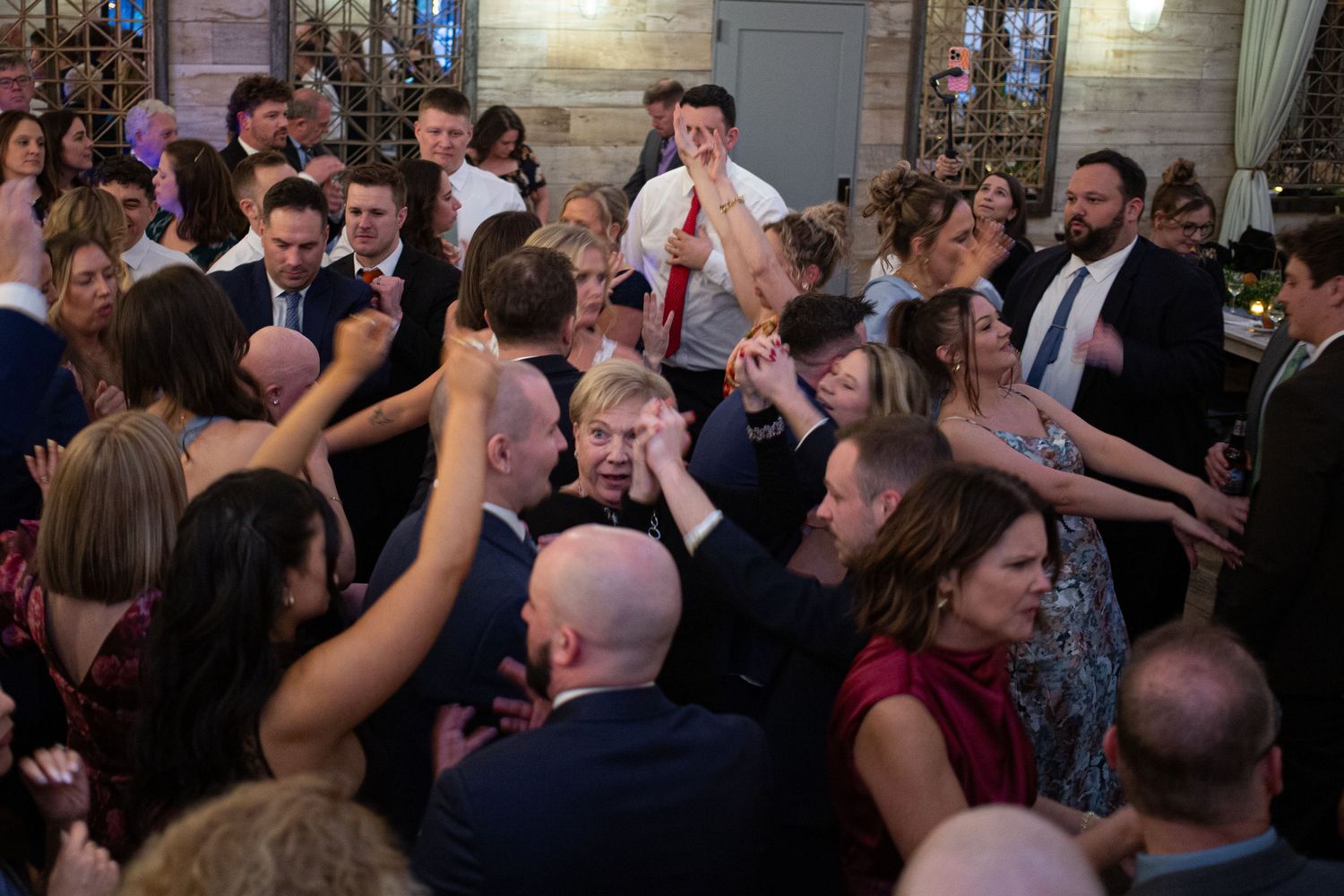 Crowded wedding reception dance floor with guests dancing and celebrating in formal attire at an elegant venue.