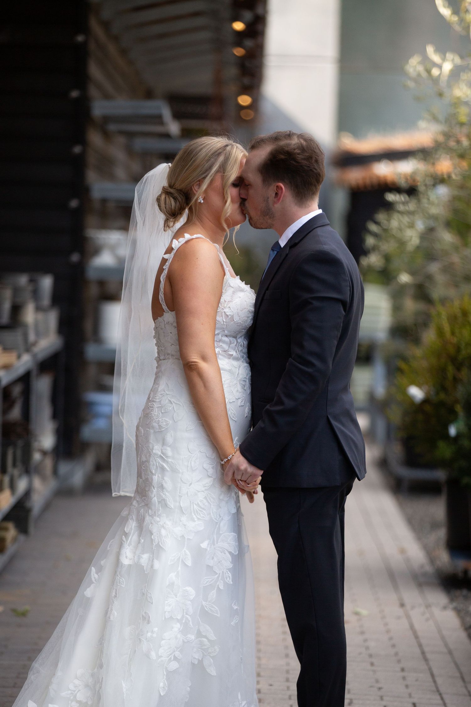 Bride and groom share a romantic moment holding hands outdoors, bride wearing lace wedding gown with veil.