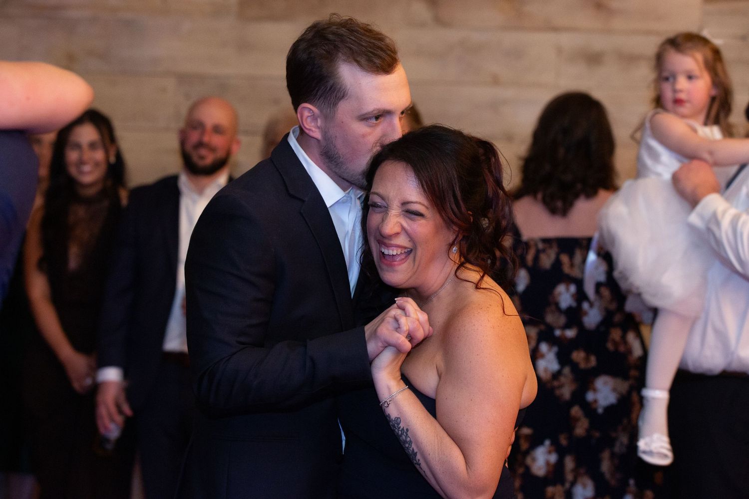 Couple dancing and laughing joyfully at a wedding reception with guests celebrating in the background.