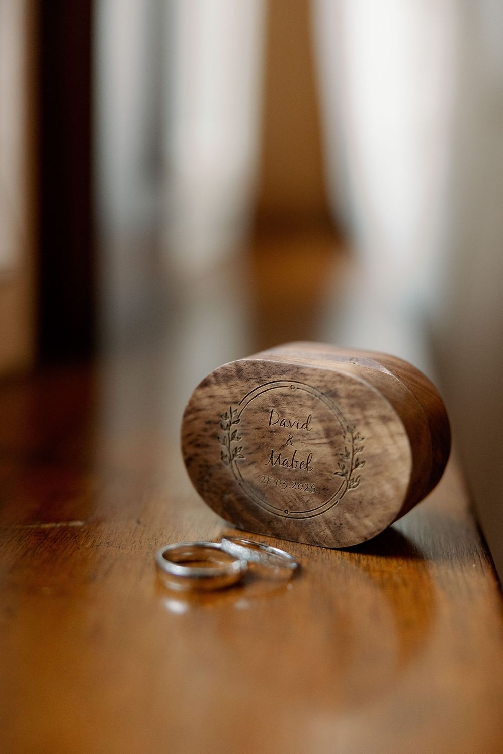 Engraved wooden wedding ring box with two silver bands on a wooden surface.