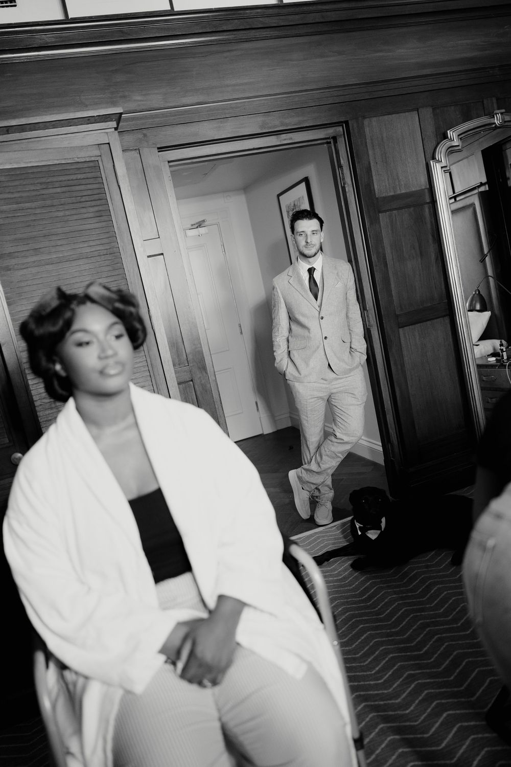 Black and white photo of bride in robe and groom in suit sharing a first look moment in hotel room.