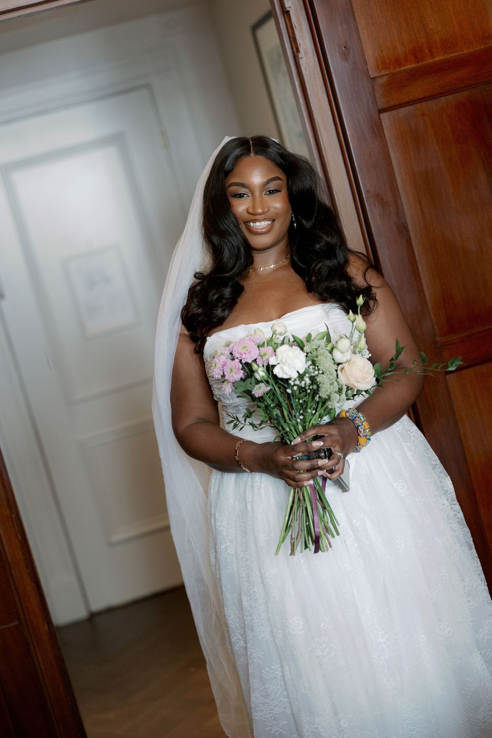 Radiant Black bride in a strapless white tulle gown holding a pastel bouquet with a cathedral veil.