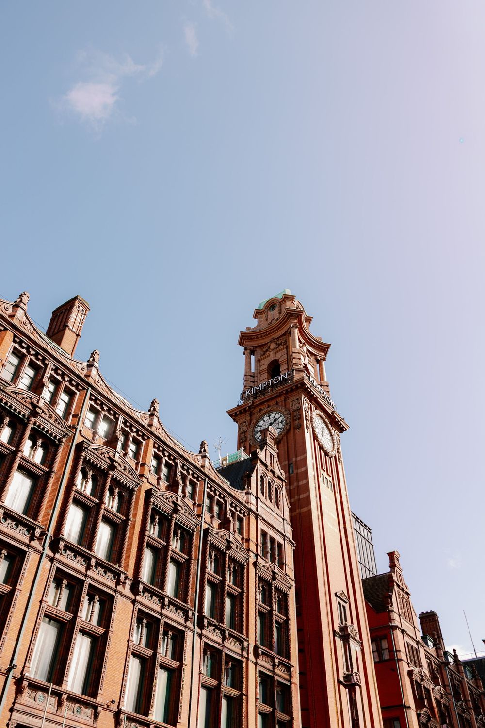 Victorian red brick building with ornate clock tower against a clear blue sky in Manchester.