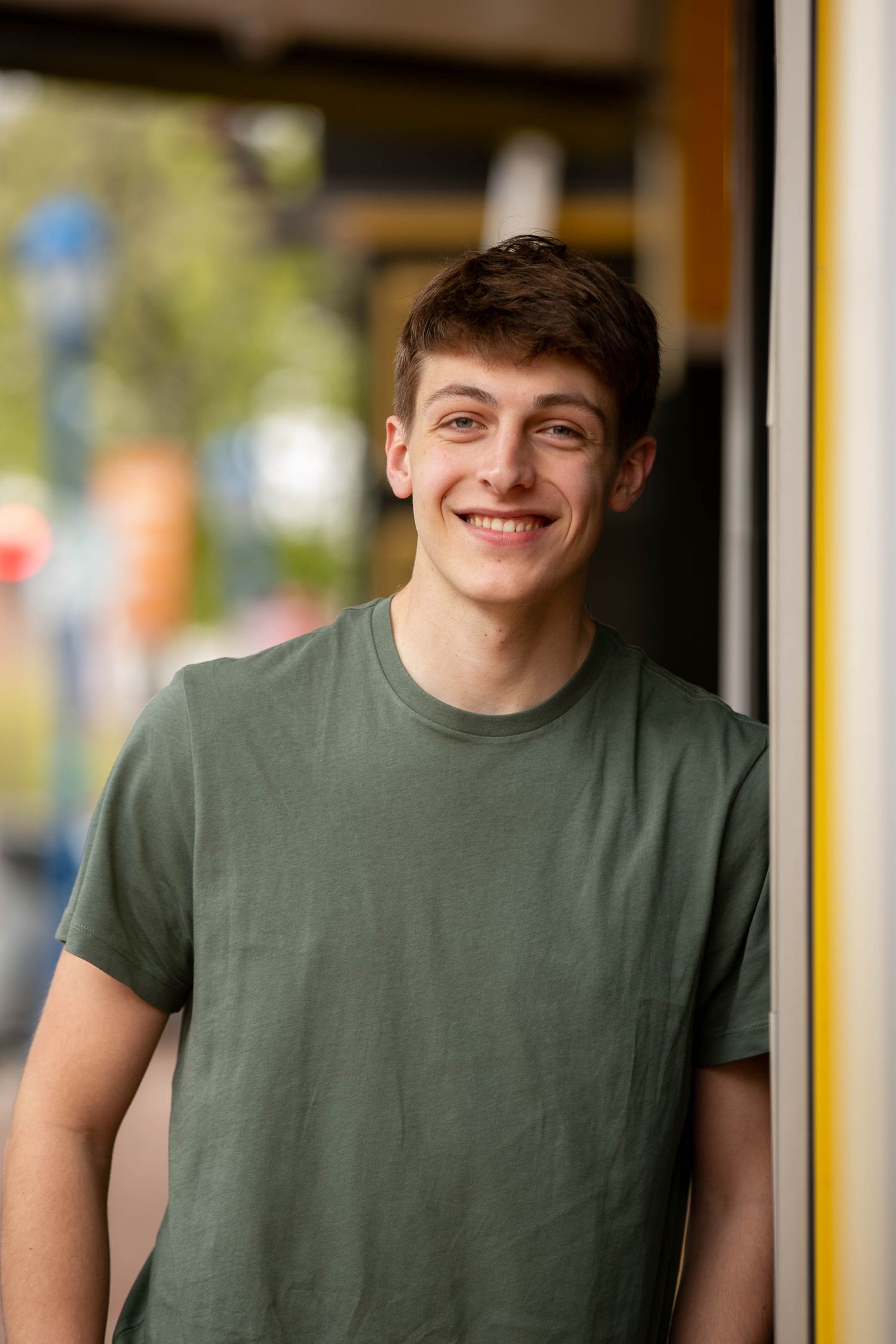 Smiling young man in green t-shirt leaning against yellow post outdoors.