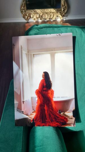 A figure in a flowing red dress sits by a bright window in a dramatic fashion photoshoot sequence.