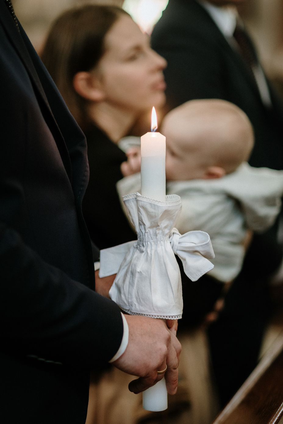 A white candle adorned with a delicate white bow being held during a formal ceremony.