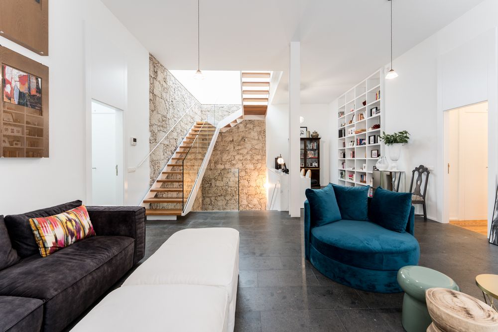 Modern white interior with stone walls features a teal blue sofa and sleek staircase design.