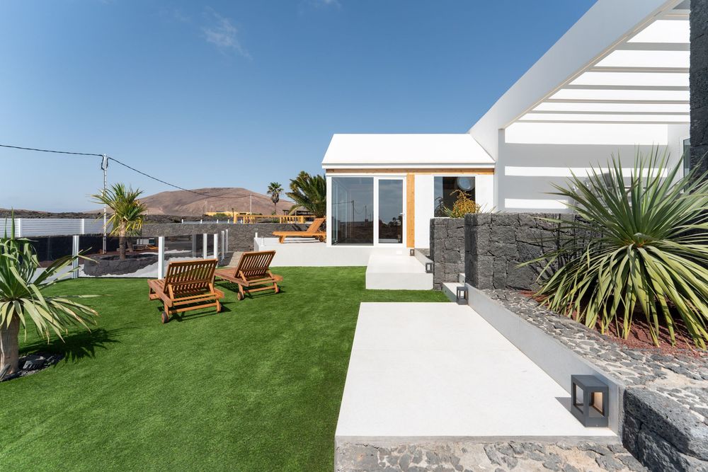 Modern outdoor seating area with wooden benches and coastal landscaping along a white wall pathway.