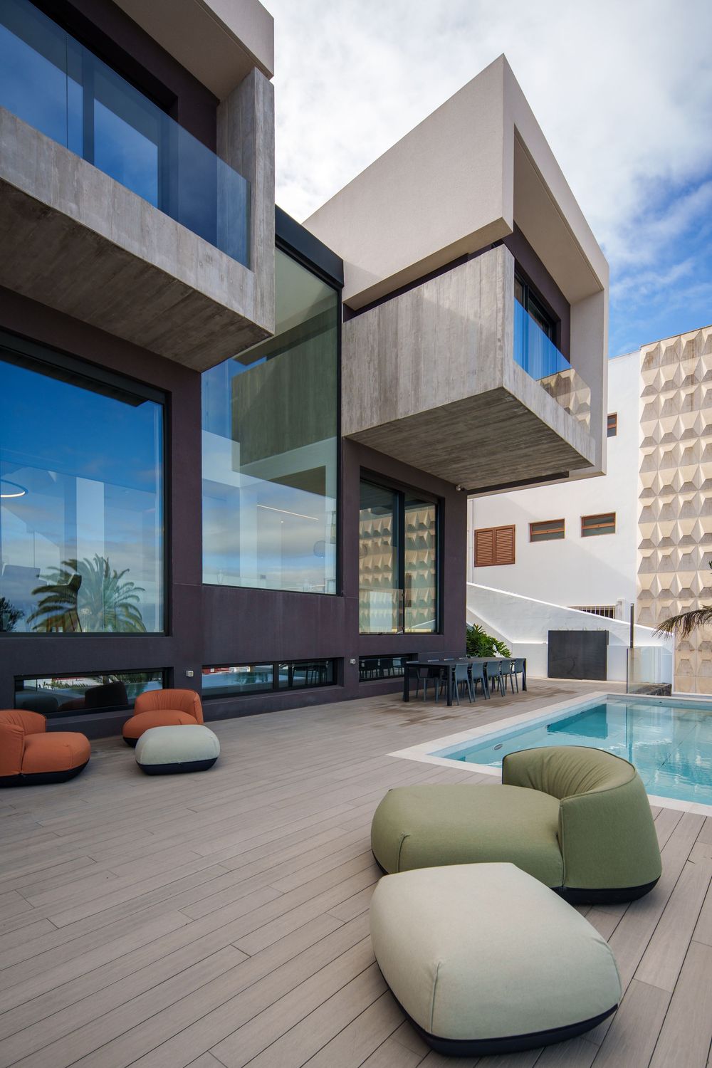 Modern luxury villa terrace with curved outdoor seating and swimming pool overlooking coastal views through glass walls.