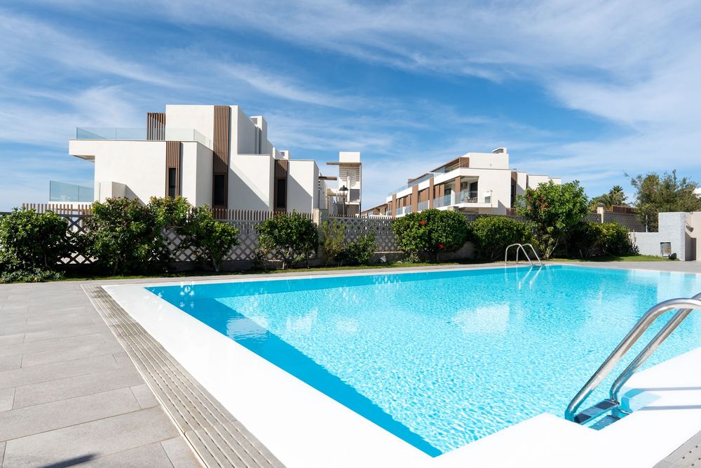 Bright blue swimming pool with modern white buildings and clear sky in the background at a luxury resort property.
