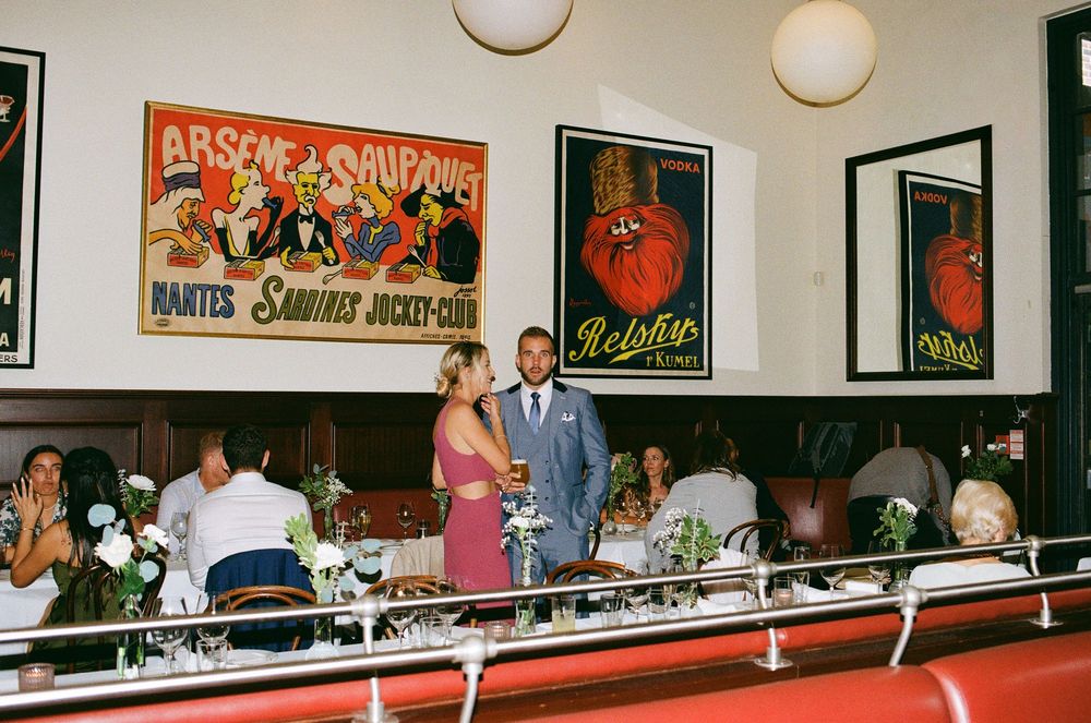 Couple shares a moment at a stylish restaurant reception adorned with vintage French posters and guests dining.