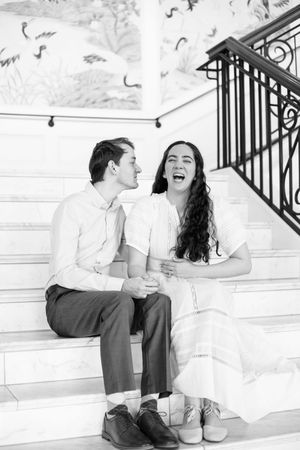 Couple sitting on white steps sharing a candid laughing moment together.