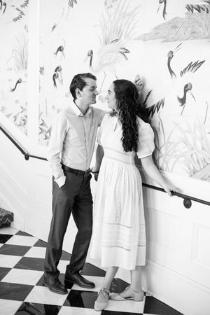 Couple in casual attire posing playfully against a decorative wall with floral patterns.