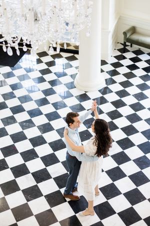 Couple dancing on a black and white checkered floor in an elegant interior space.