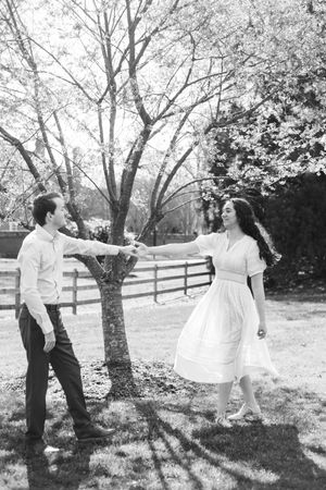 A romantic black and white photo of a couple dancing together outdoors under blooming spring trees.