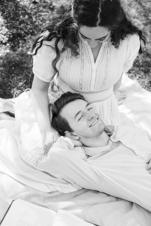 A tender black and white romantic moment between two people lying together in soft white fabrics.