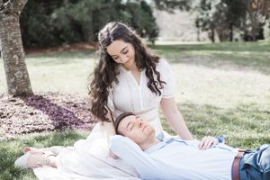 A couple relaxes together on a blanket in a sunny park setting during a romantic outdoor photoshoot.