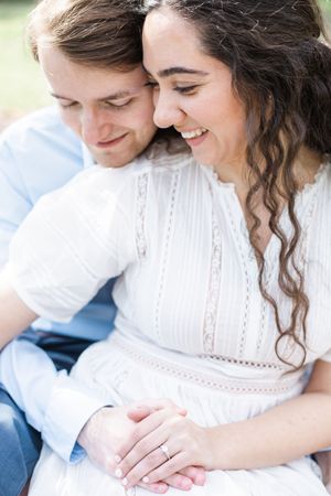 A romantic couple embraces outdoors in soft lighting wearing white and blue clothing during an intimate photoshoot.