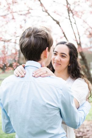 Couple embracing under blooming cherry blossom trees in springtime.