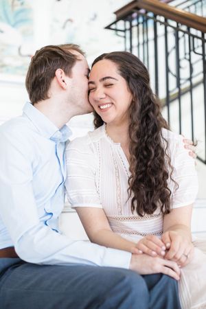 A couple shares intimate laughing moments during an outdoor engagement photo session on concrete steps.