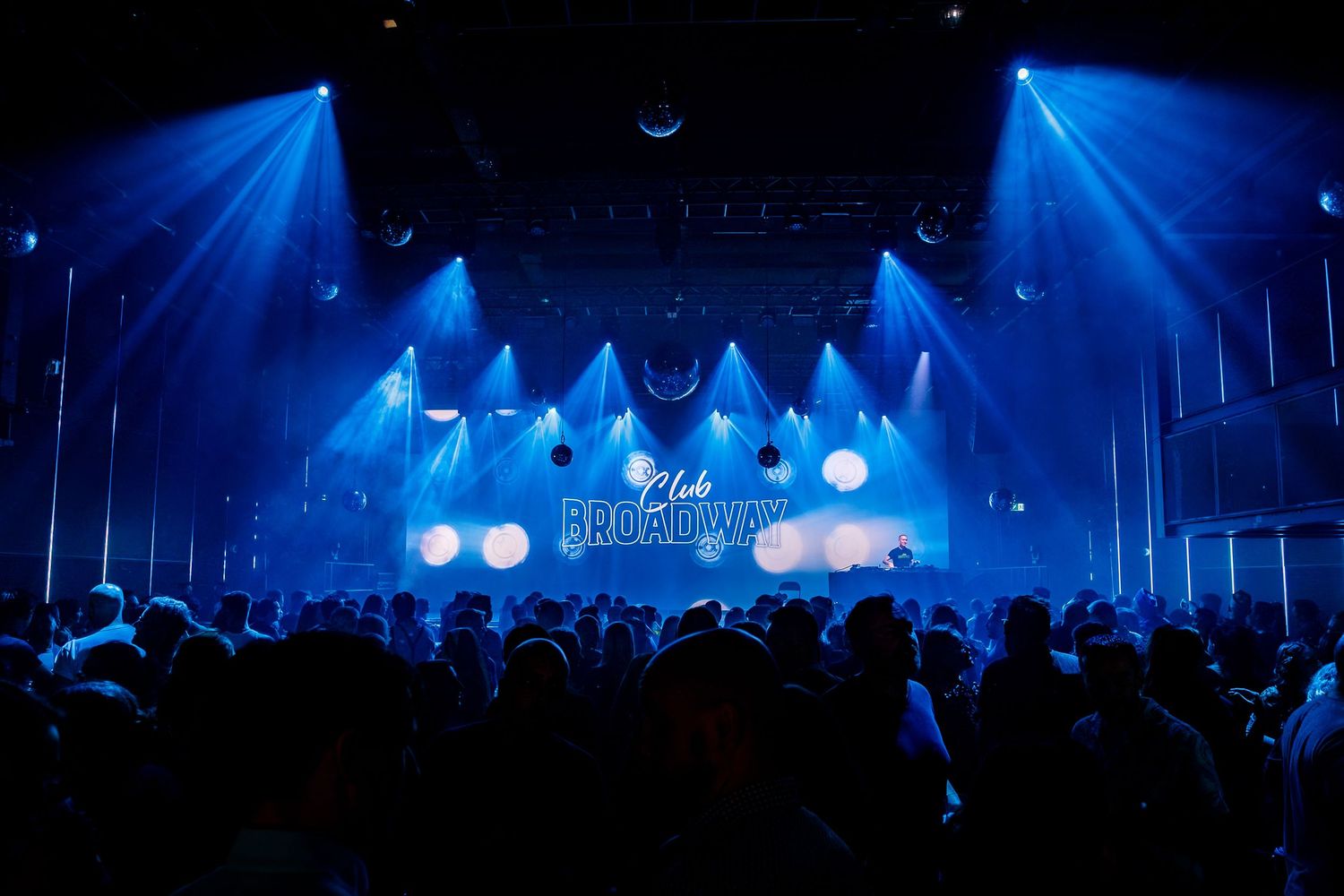 Concert venue lighting setup with blue spotlights creating atmospheric beams in dark space.