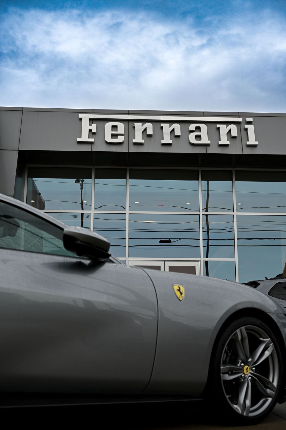 A sleek gray Ferrari sports car parked in front of a Ferrari dealership with the brand name displayed on the building.