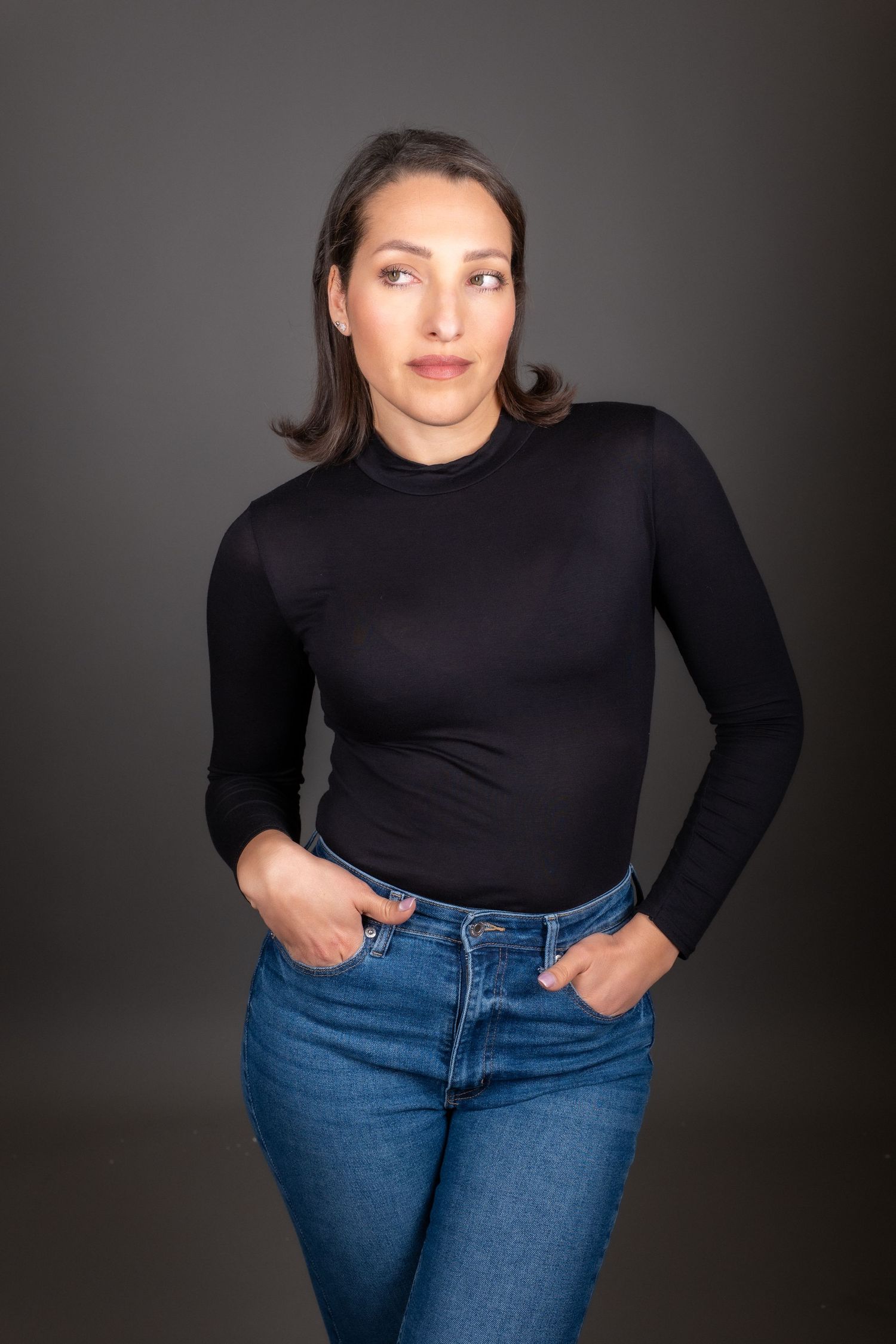 Portrait of someone in a yellow sleeveless button-up shirt and jeans posing with a warm smile against a dark background.