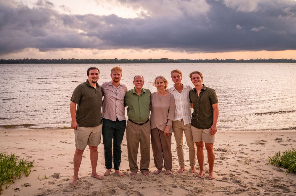 Group of people enjoying sunset together on a sandy beach with water and cloudy sky in the background.