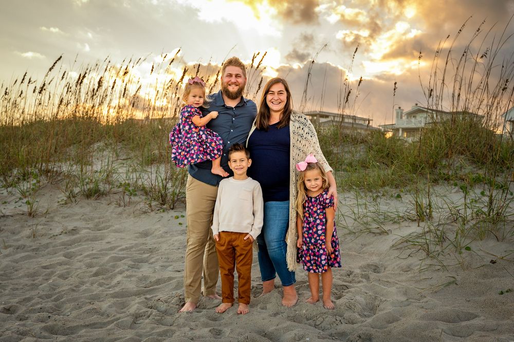 A group poses together on a sandy beach dune at sunset with sea oats swaying in the golden light.