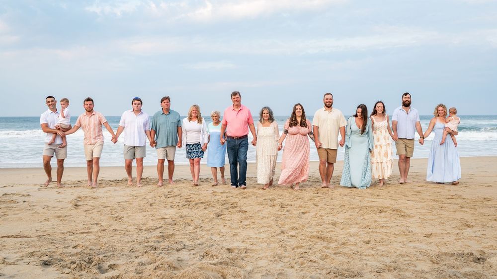 Group of people wearing light colored clothing walking together on a sandy beach during sunset.