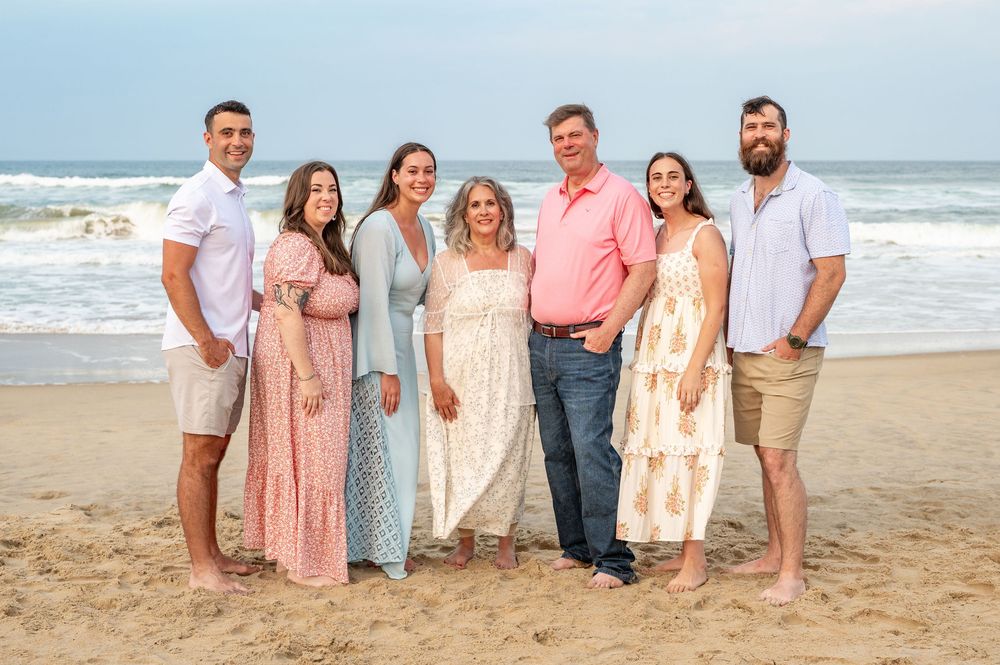 A family group wearing coordinated coral and neutral outfits poses together for photos on a sunny beach.