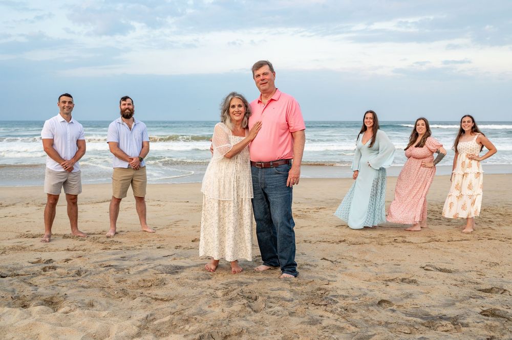 Family members pose together on a sandy beach wearing coordinated pastel outfits during a sunset photo session.