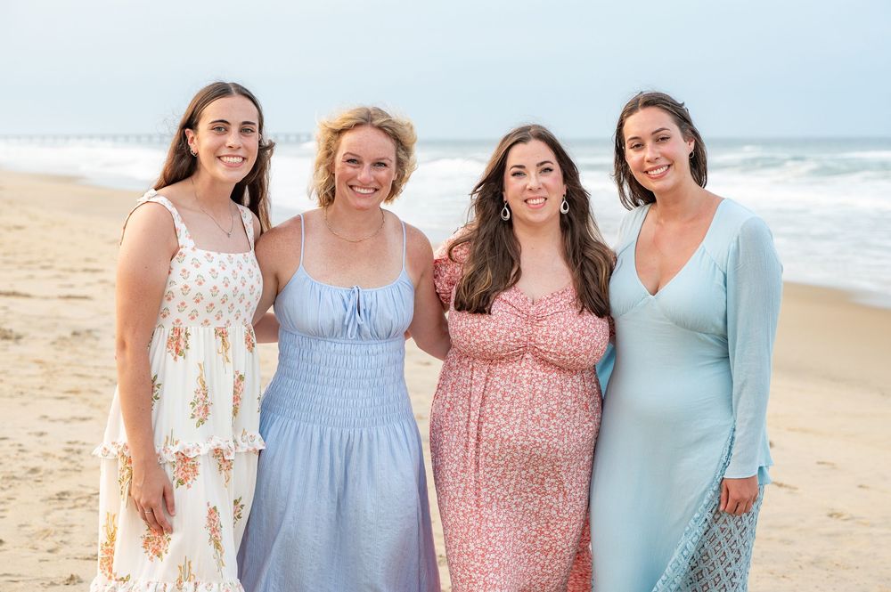 A group wearing coordinated pastel blue and pink dresses pose together on a sunny beach.