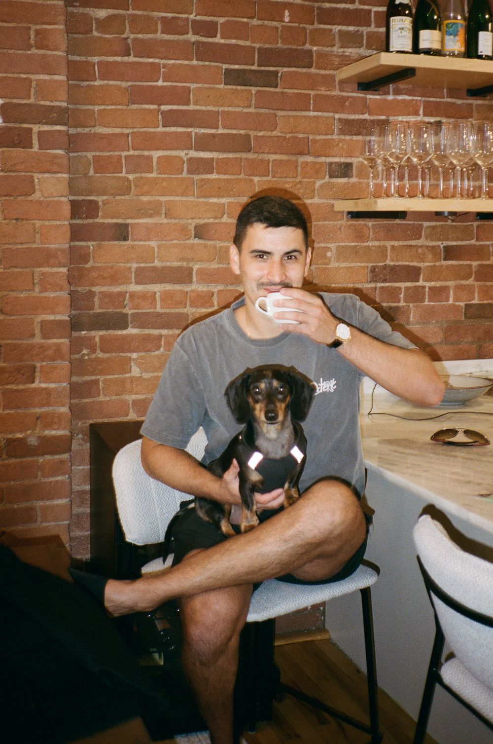 Groom drinking coffee while holding a small dachshund puppy on wedding morning in Old Montreal. Candid Montreal Wedding Photography by Aliza