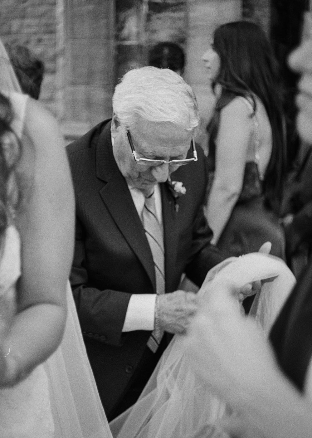 Grandpa of the bride in suit adjusting bride's veil at wedding ceremony, black and white photo. Candid Montreal Wedding Photography by Aliza
